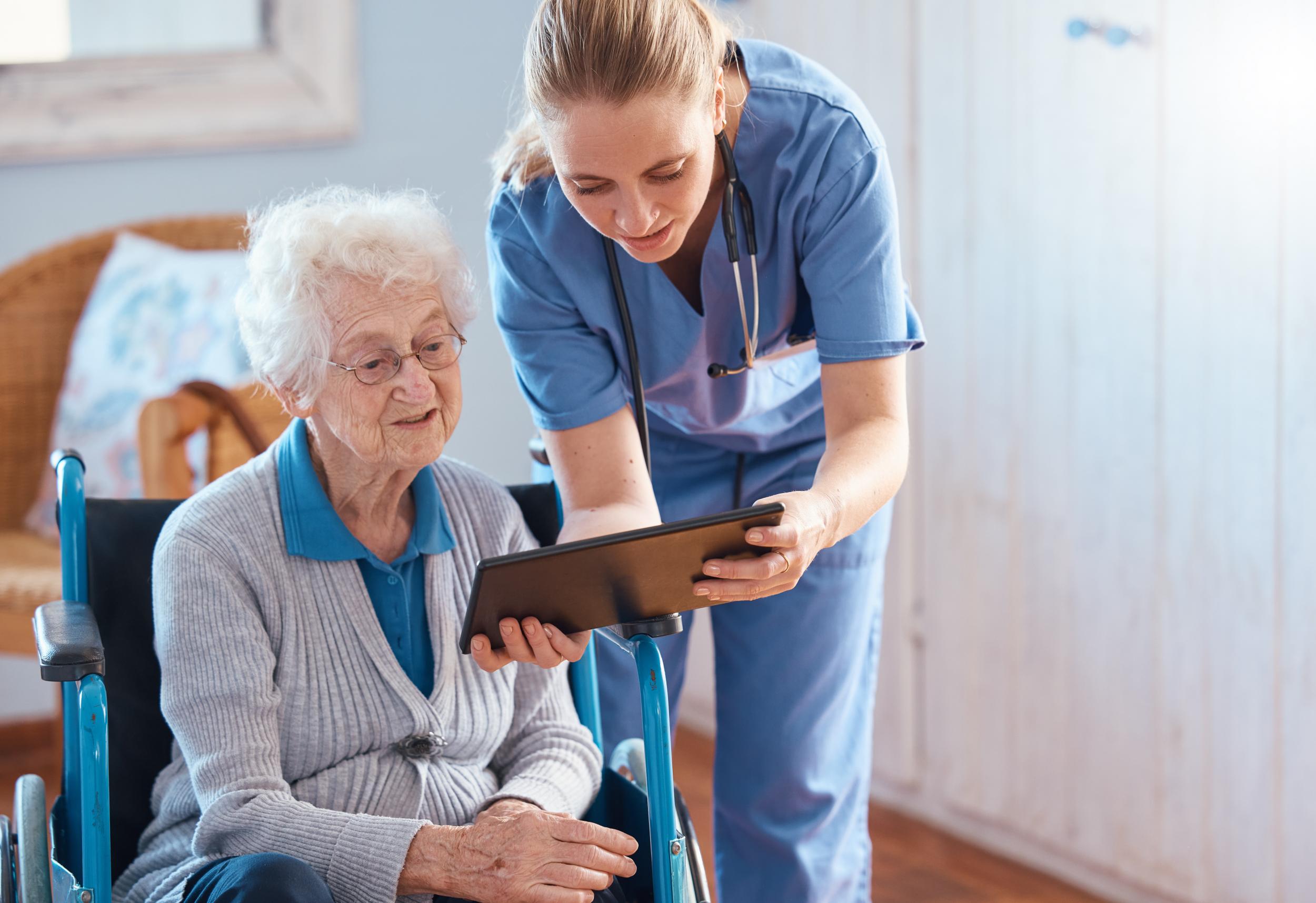 female nurse reviews information on a tablet with an elderly female patient